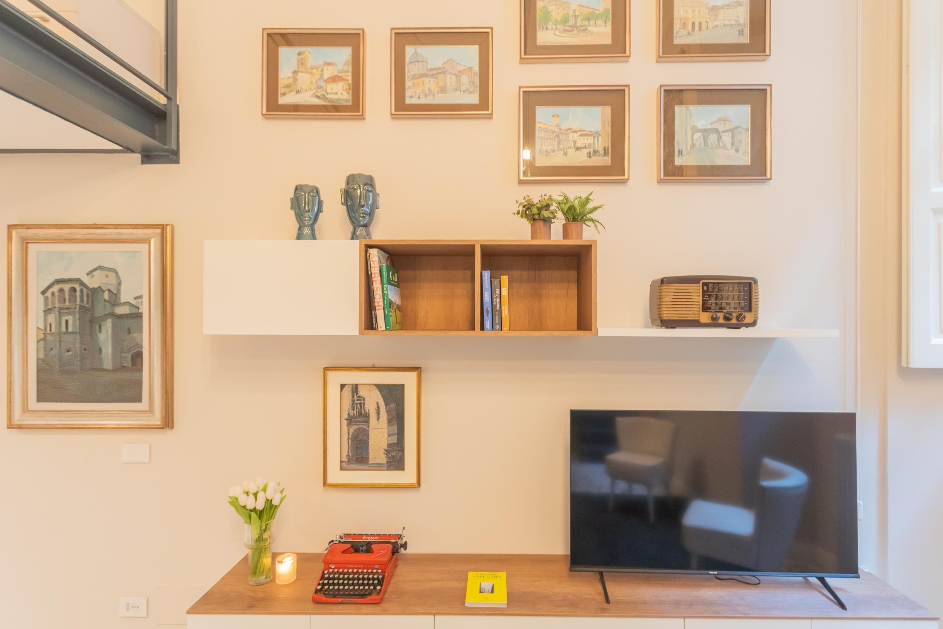 A living room with a flat-screen TV, a wooden coffee table, a red typewriter, and a bookshelf with books and decorative items.