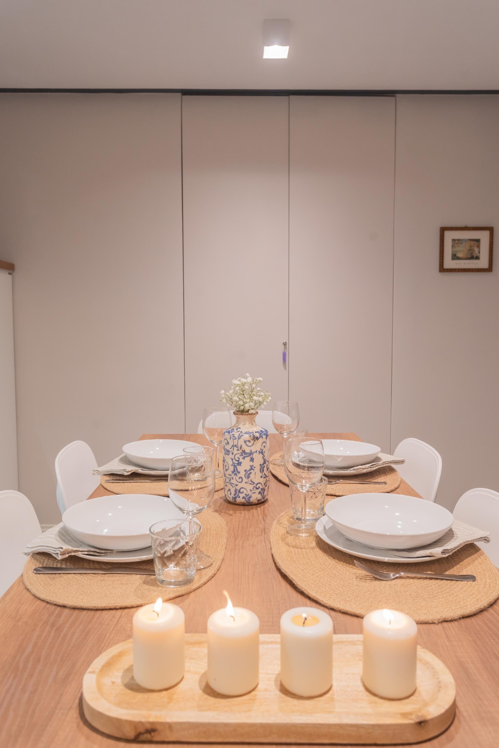 A dining table set with white plates, glasses, and candles, with a vase of flowers in the center.