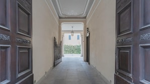 Un pasillo con puertas de madera oscura, paredes de color claro y piso de baldosas que conduce a una ventana con vista a vegetación.
