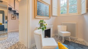 Una habitación con chimenea, una silla blanca, un cuadro enmarcado y una ventana con vistas a vegetación.