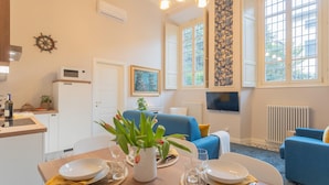 Una sala de estar moderna con un sofá azul, una mesa de comedor preparada para cuatro personas y una cocina con microondas y fregadero.