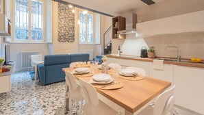 A modern kitchen with a dining area, white cabinets, and a blue sofa. - Cinque Giornate 70 Suites (Como)