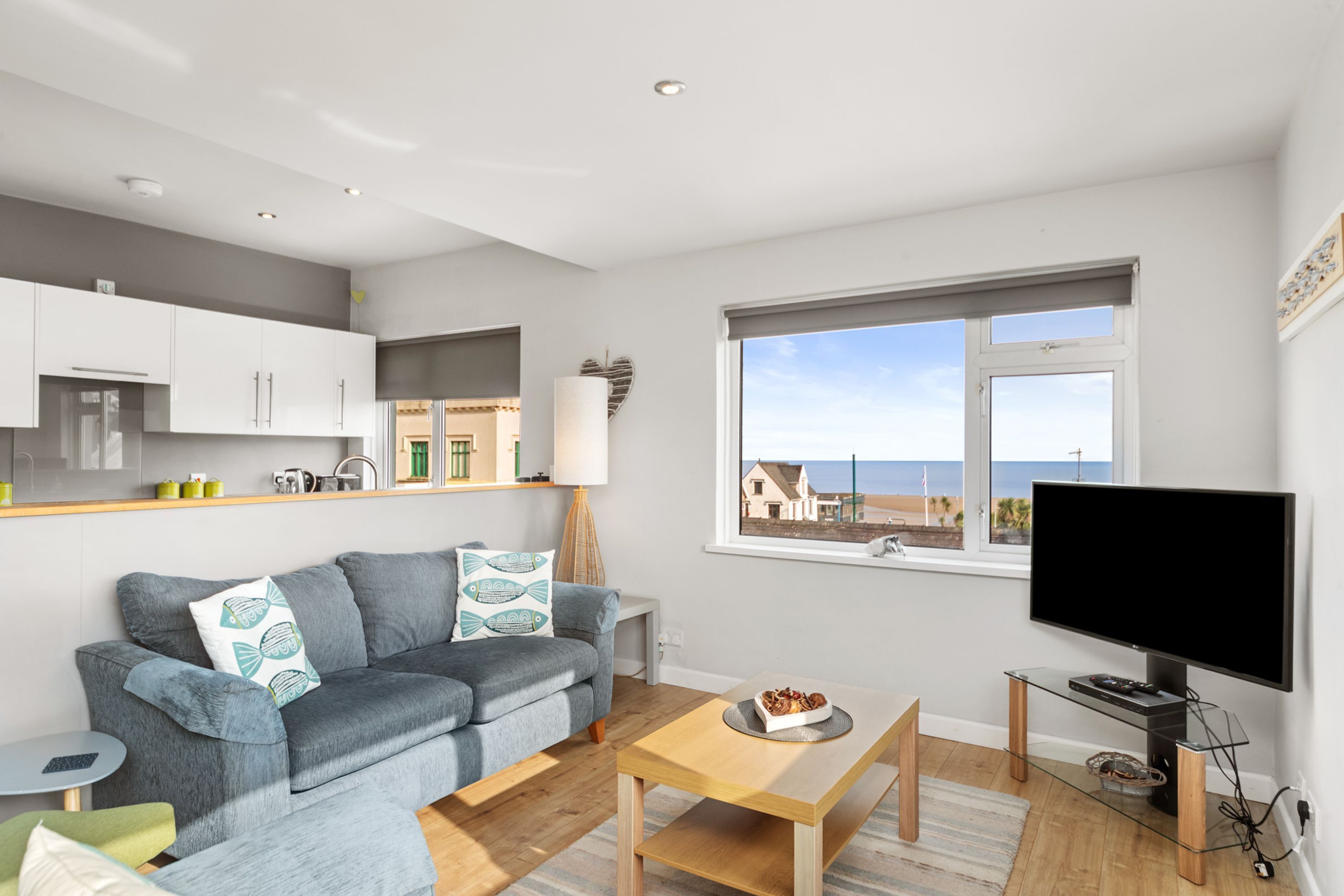 A modern living room with a grey sofa, a wooden coffee table, and a TV on a stand.