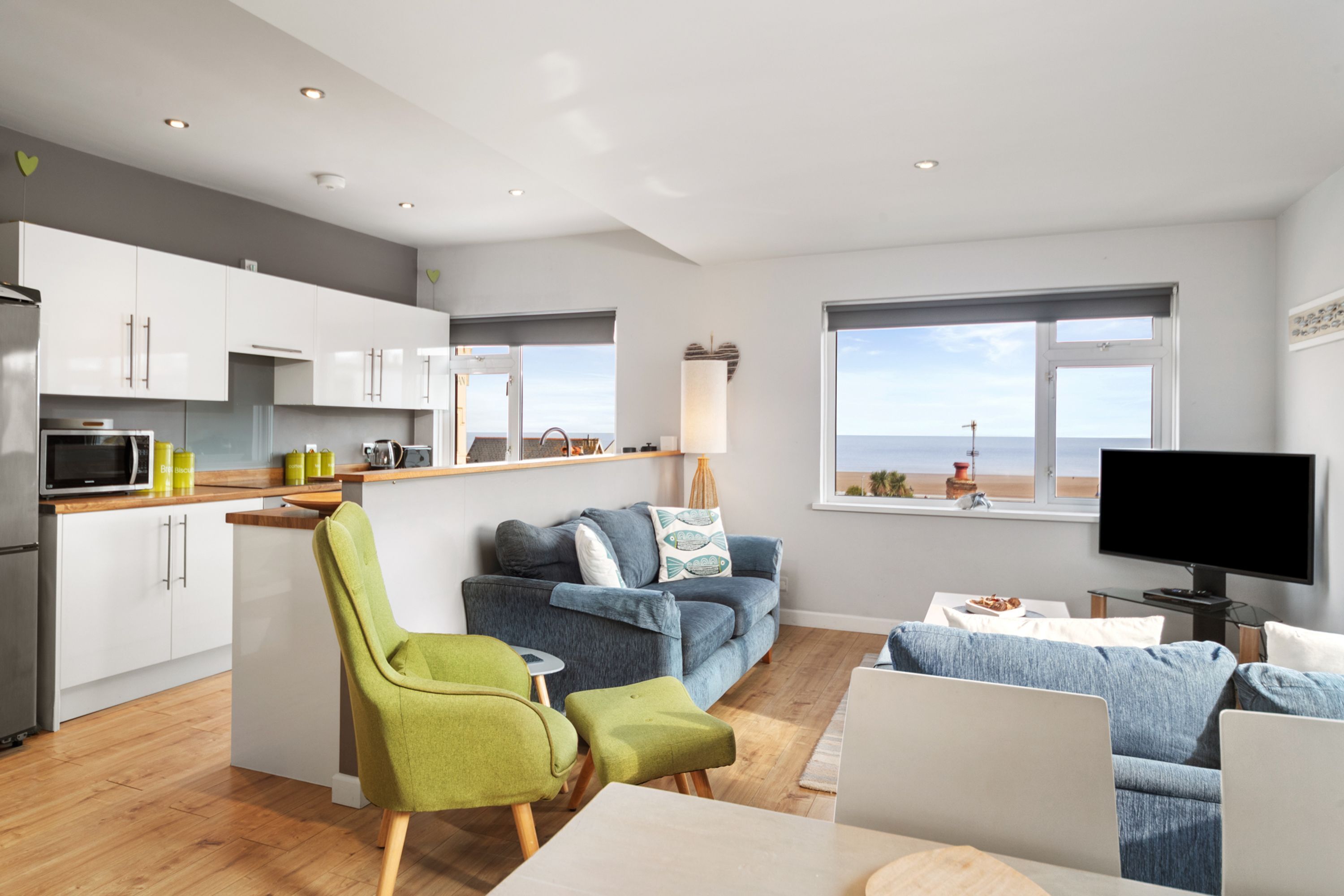A modern living space with a kitchen, dining area, and seating by a large window with a view.