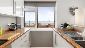 Une cuisine moderne avec vue sur la plage, des armoires blanches et un plan de travail en bois.