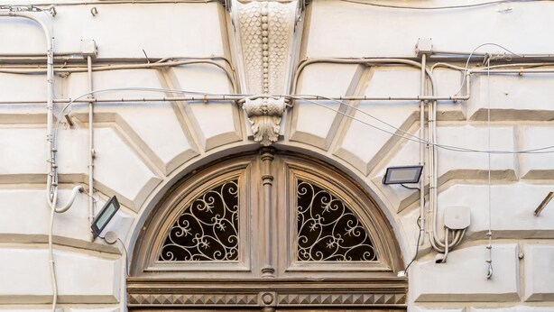 A large, ornate wooden door with a decorative arch above it, set in a building with a textured facade and numbered plaques. - Duomo Grand Family Loft (Naples)