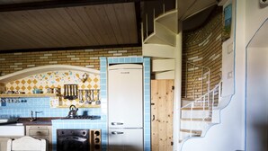 Eine Küche mit Herd, Spüle und einem weißen Kühlschrank. Es gibt eine Holztreppe und eine geflieste Wand mit Rautenmuster.