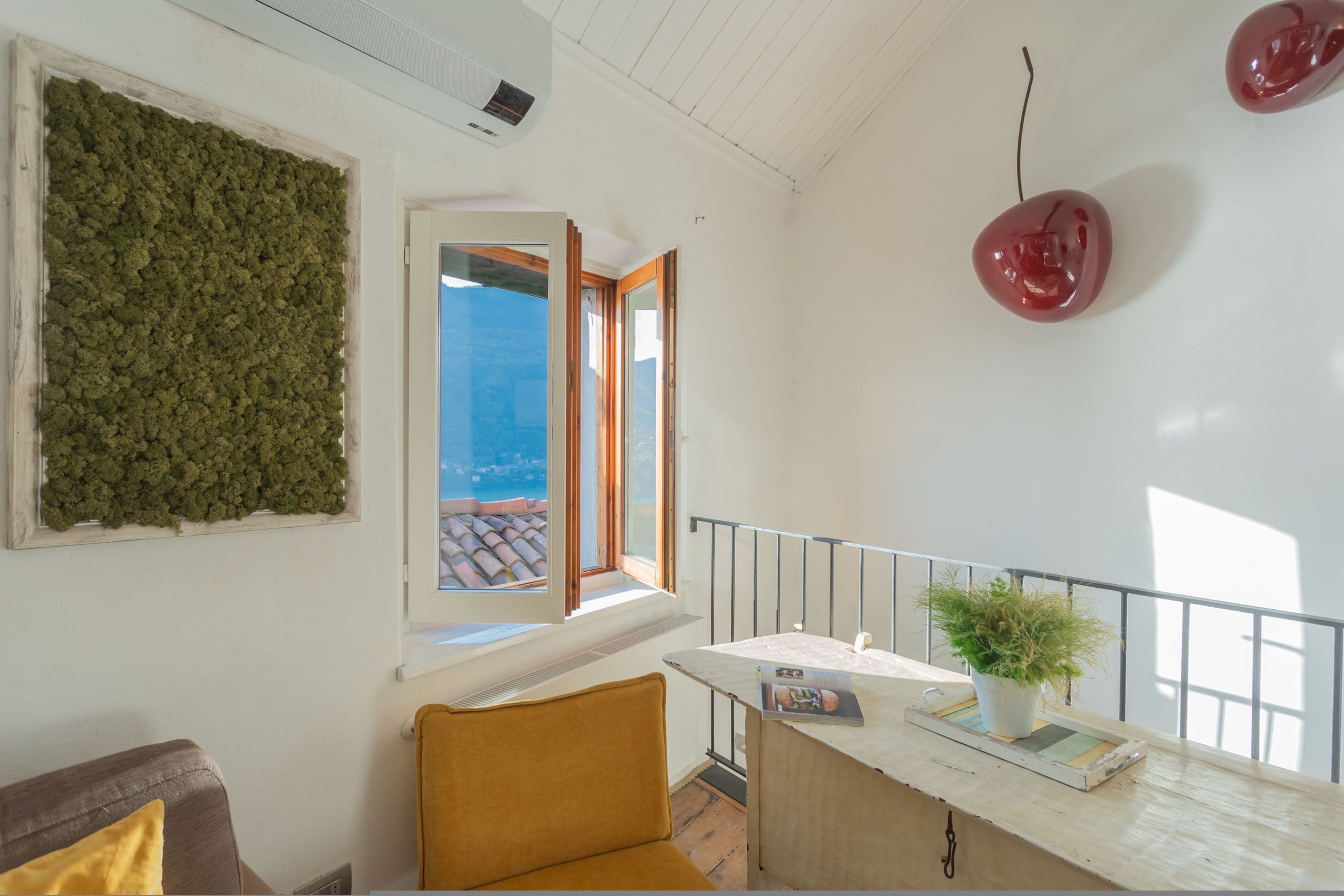 A room with a view of the sea, a window with a view, a plant on a table, and a chair.