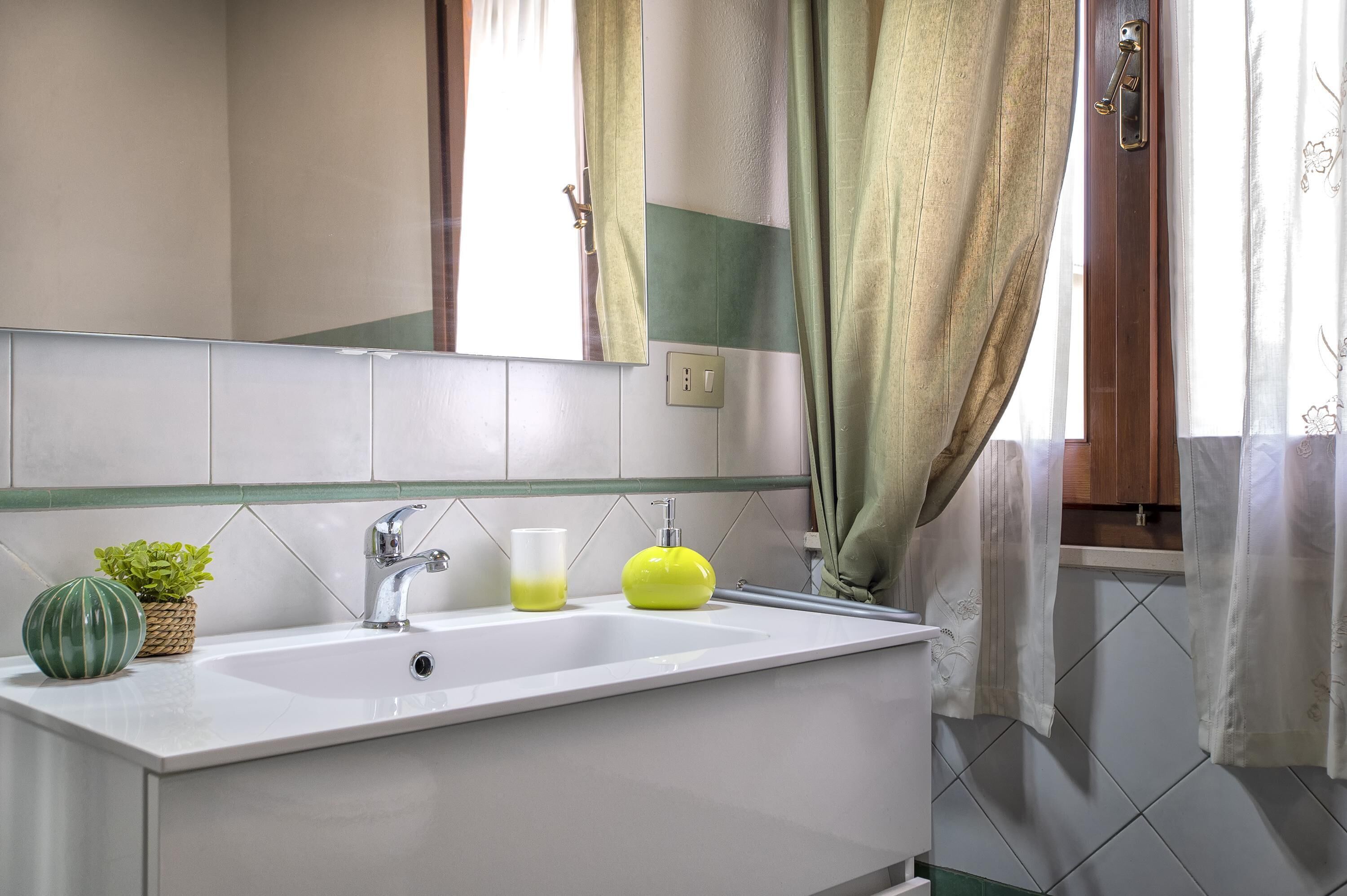 Un baño con un lavamanos blanco, una planta verde, un dispensador de jabón amarillo y un espejo.