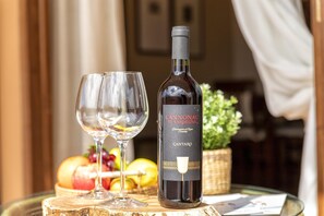 Una botella de vino CANTARO y dos copas sobre una superficie de madera, con frutas y una cesta al fondo.