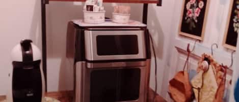 A kitchenette with a coffee maker, a microwave, and a shelf with cups and plates.