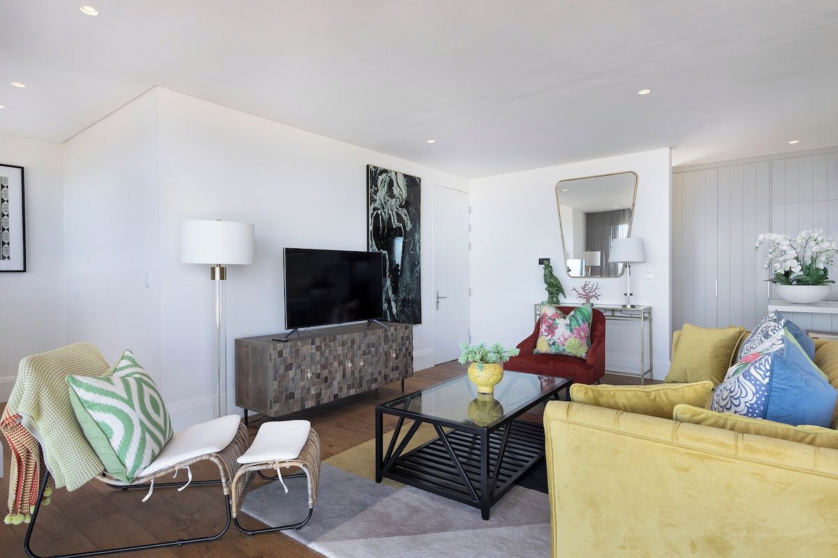 A modern living room with a flat-screen TV, a glass coffee table, and a yellow sofa.