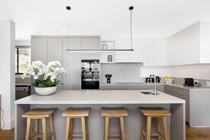 A modern kitchen with a central island, bar stools, and a potted orchid plant. - Alpha One 501 Magnificent Views no load shedding (Cape Town)