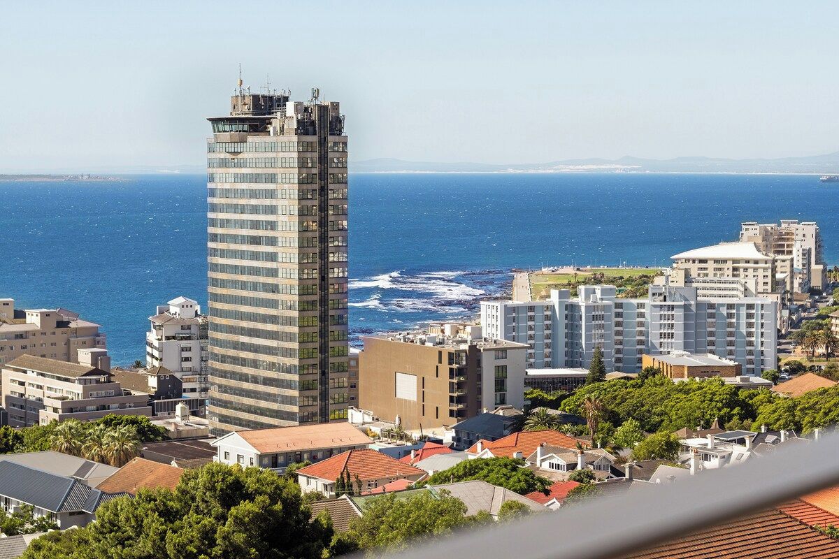 A coastal cityscape with a prominent high-rise building, smaller residential structures, and a view of the sea.
