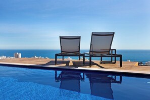 A poolside area with two lounge chairs facing a clear view of the ocean.
