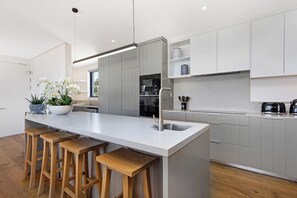 A modern kitchen with a central island, bar stools, and a potted plant.