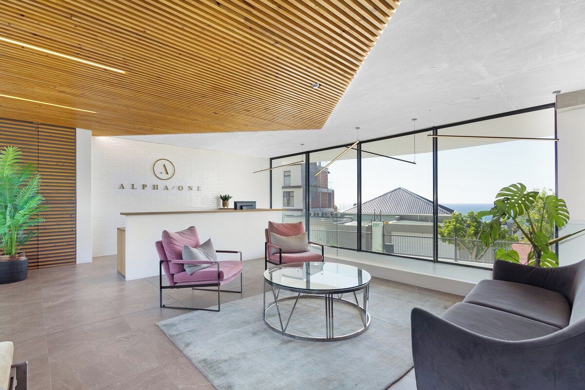 A modern interior with a wooden ceiling, a reception desk, and a seating area with a view of the city.