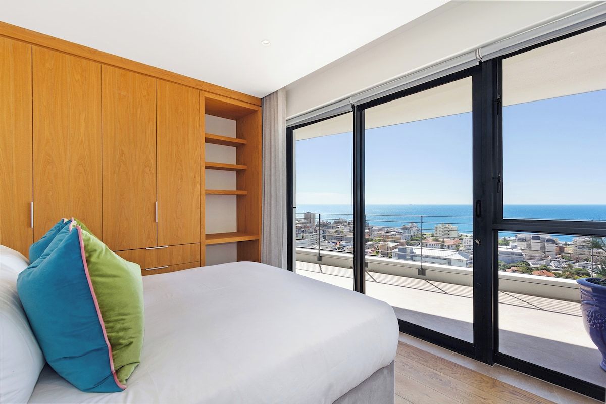 A bedroom with a large window, a bed, and a wooden wardrobe.