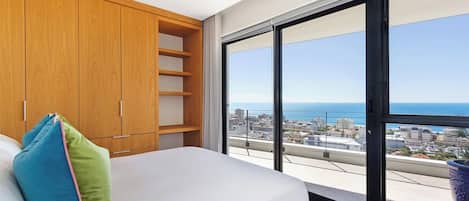 A bedroom with a large window, a bed, and a wooden wardrobe.