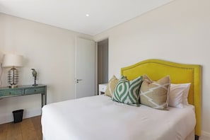 A bedroom with a bed, bedside table, lamp, and a door leading to another room. - Alpha One 501 Magnificent Views no load shedding (Cape Town)