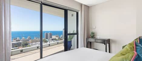 A hotel room with a large sliding glass door leading to a balcony with a city view.