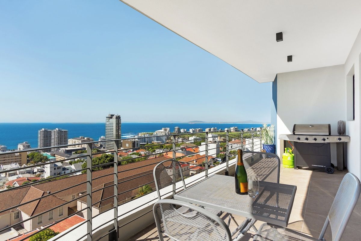 Een balkon met een tafel, stoelen, een fles en een barbecue.