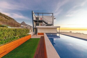 A modern building with a pool, a staircase, and a view of the ocean.