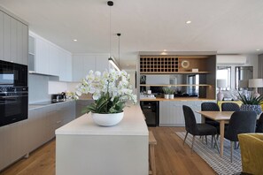 A modern kitchen with white cabinetry, a central island with a white orchid centerpiece, and a dining area with a wooden table and chairs.