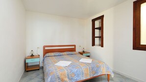 Ein kleines, sauberes Schlafzimmer mit einem Einzelbett, zwei Nachttischen und einem Fenster mit Holzrahmen.