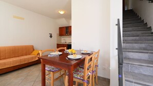 A dining area with a wooden table and chairs, a sofa, and a kitchen in the background. - Beautiful apartment for 4 guests with terrace (Valledoria)