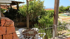 A patio with a wooden pergola, a stone wall, and a view of the sea. - Beautiful apartment for 4 guests with terrace (Valledoria)
