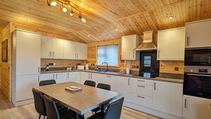 A modern kitchen with wooden ceiling, white cabinets, a dining table with chairs, and built-in appliances. - Ferry Lodge - Norfolk Broads (Brundall)