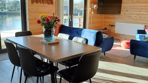 A modern interior with a wooden dining table, black chairs, a blue sofa, and a TV mounted on the wall. - Ferry Lodge - Norfolk Broads (Brundall)