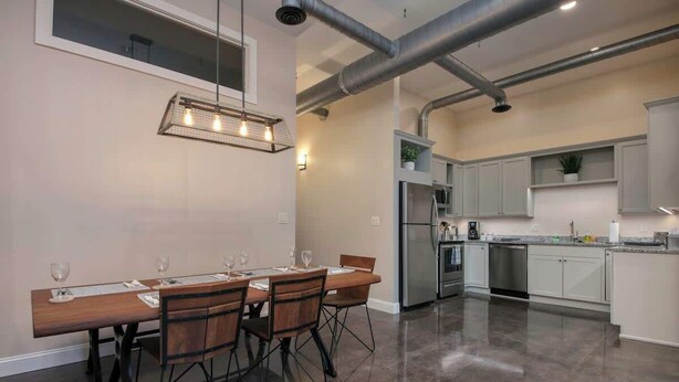 A modern kitchen with a dining area, stainless steel appliances, and a large window. - Stay Roanoke | Bright modern loft for adventurers (Roanoke)