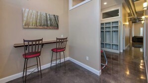 A hallway with a dark floor, a painting on the wall, and a white storage unit with shelves. - Stay Roanoke | Bright modern loft for adventurers (Roanoke)