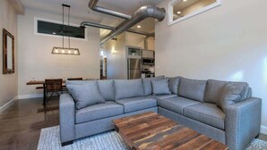 A modern living room with a grey sectional sofa, a wooden coffee table, and a dining area with a wooden table and chairs. - Stay Roanoke | Bright modern loft for adventurers (Roanoke)
