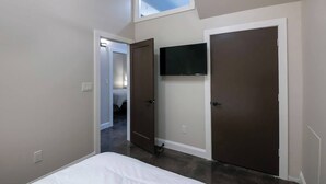 A bedroom with a bed, a TV mounted on the wall, and two doors. - Stay Roanoke | Bright modern loft for adventurers (Roanoke)