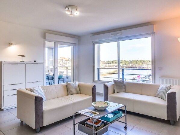 A modern living room with two sofas, a coffee table, and a view of a marina through large windows.