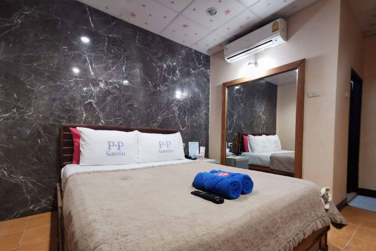 A hotel room with a marble wall, a bed with a beige blanket, two pillows with 'P.P' branding, a blue towel, and a remote control.