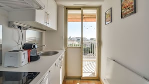 A compact kitchen with a toaster, kettle, and sink. A sliding glass door leads to a balcony with a view of the city.