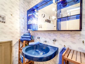 Bathroom features a blue sink, large mirror, and a wooden stool with a towel.
