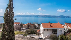 A coastal residential area with houses, a stone wall, and a view of the sea and mountains.