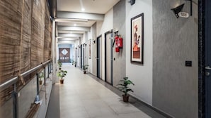 Corredor de hotel com plantas em vasos, extintores de incêndio e portas numeradas.