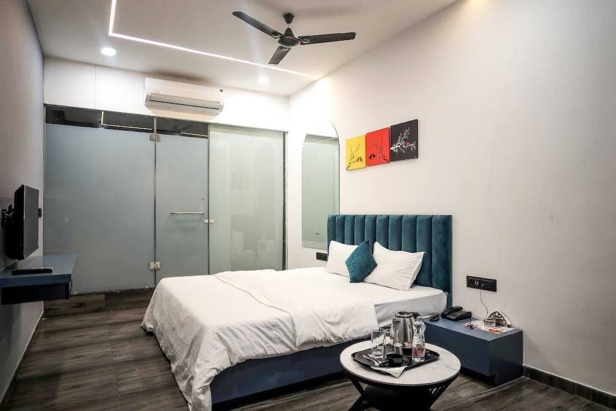 Ein modernes Hotelzimmer mit einem Bett, einem Nachttisch mit Telefon und Brillen, einem kleinen runden Tisch mit Tablett, einem Deckenventilator und einer Wand-Klimaanlage.