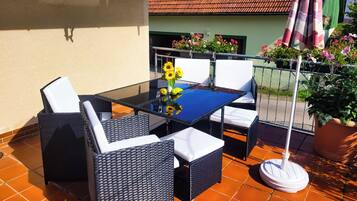 A patio with a glass table, wicker chairs, and a potted plant.