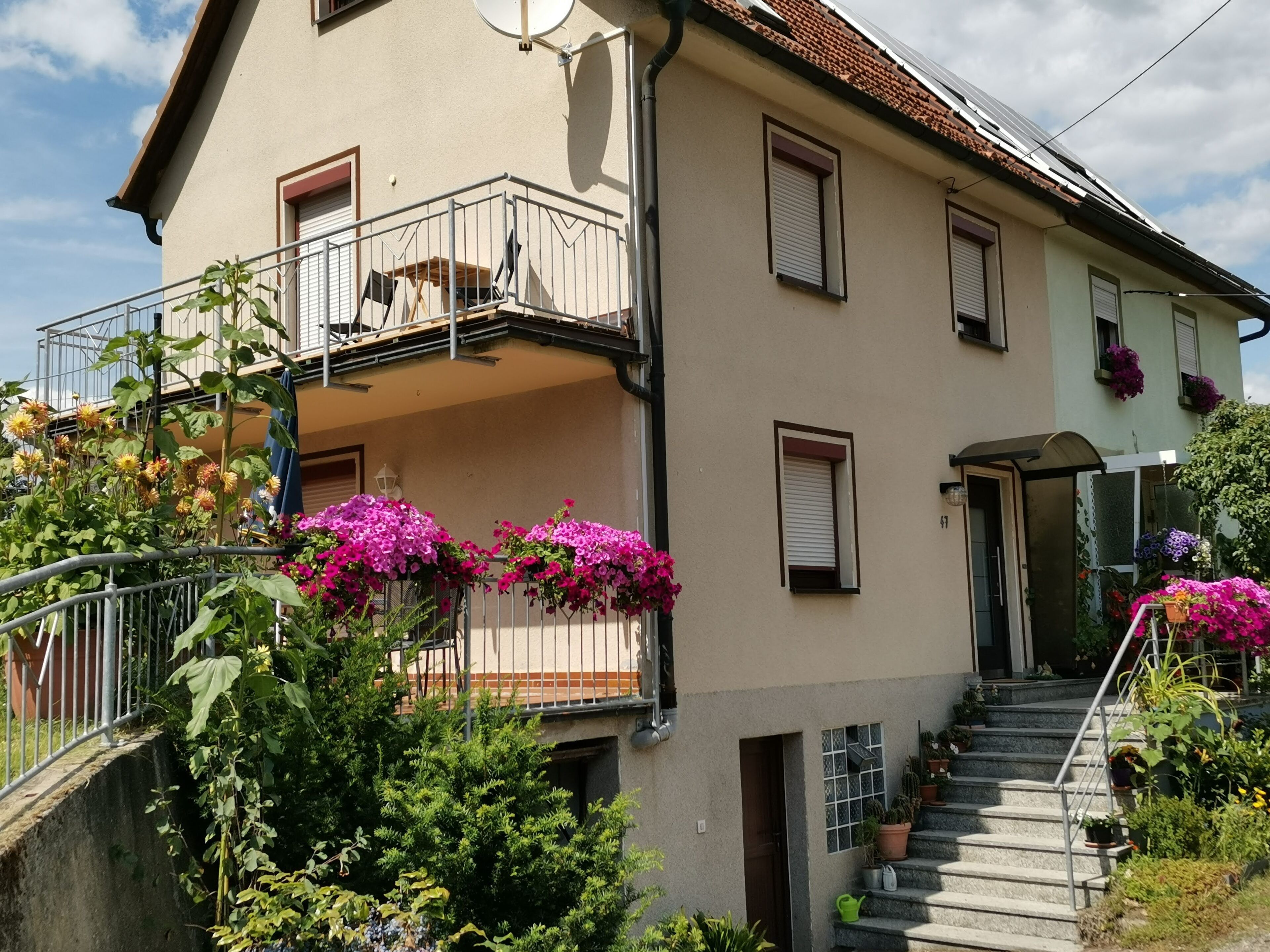 A two-story house with a balcony, a staircase, and potted plants.