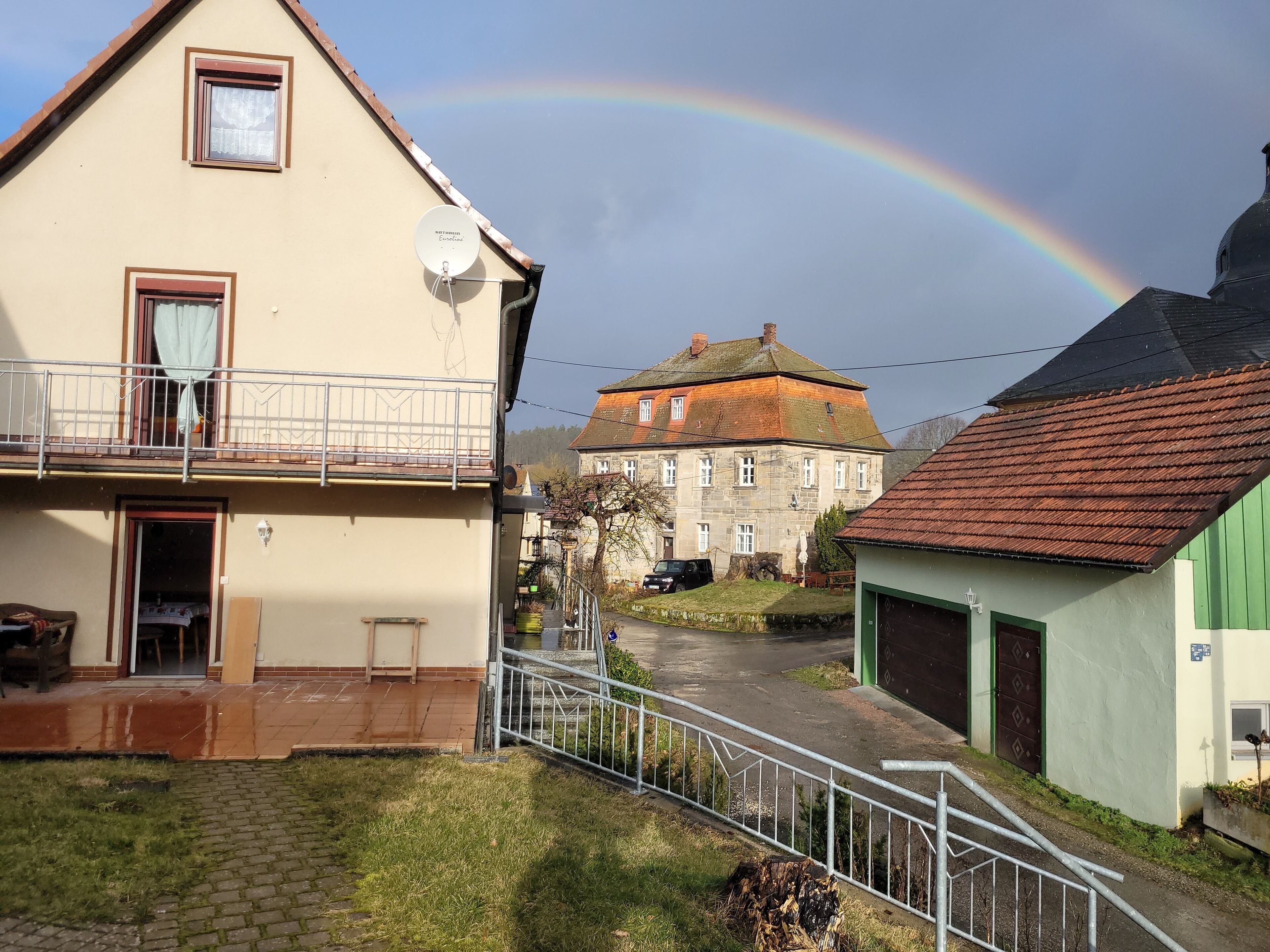 Un quartier résidentiel avec une maison dotée d’une antenne parabolique, d’un balcon et d’un garage vert.