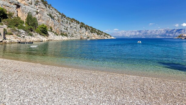 A pebble beach with clear blue water, rocky cliffs, and a distant mountain range. - Nice apartment for 2 guests with WIFI, A/C, TV and terrace (Pokrivenik)