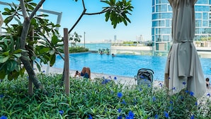 A pool area with a view of a city skyline, surrounded by greenery and a modern building.