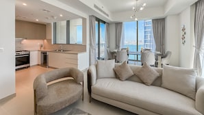 A modern living room with a sofa and armchair, a dining area with a table and chairs, and a kitchen with a stove and sink.